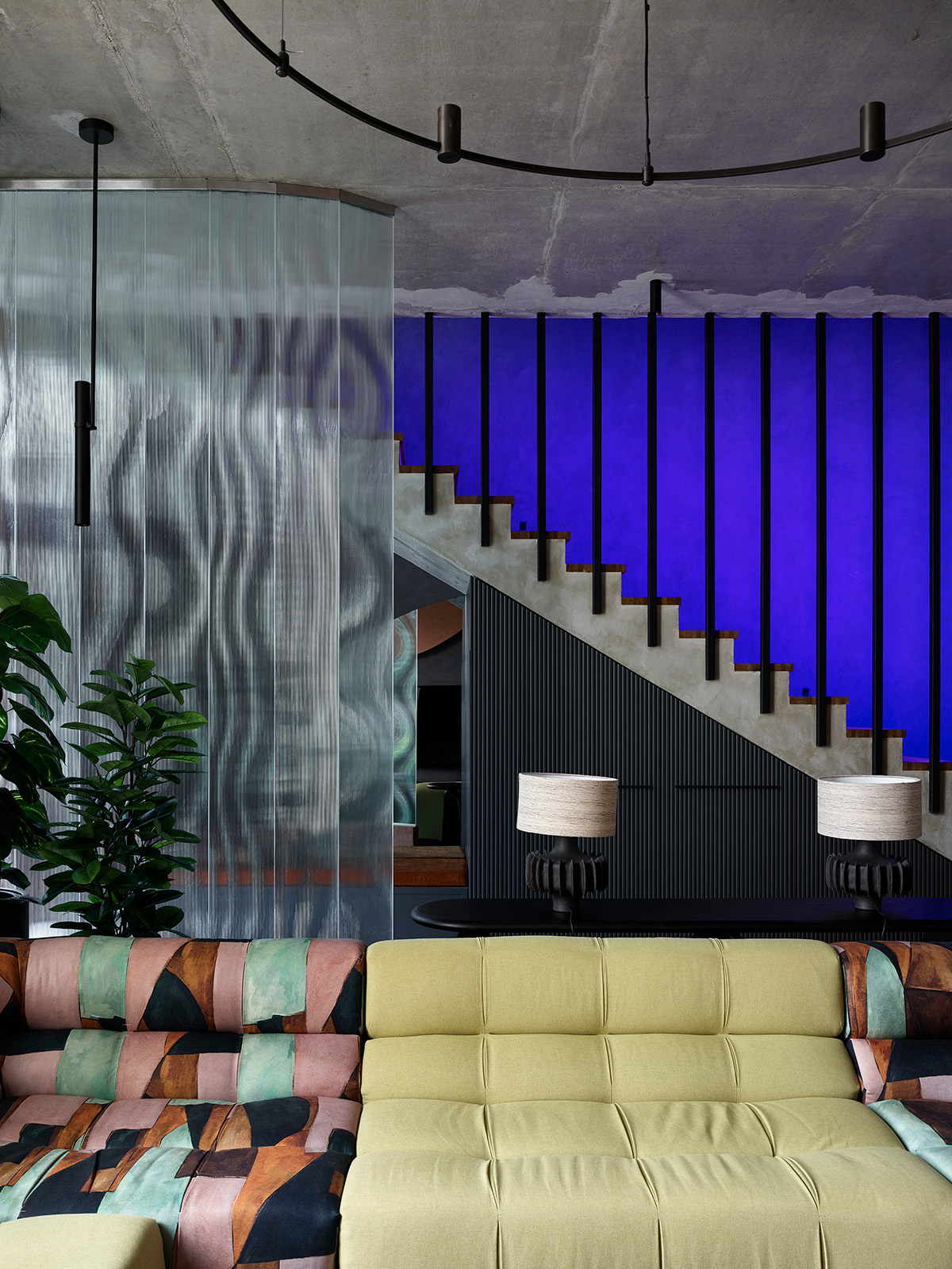 Salón con escalera retroiluminada en azul y sofá verde