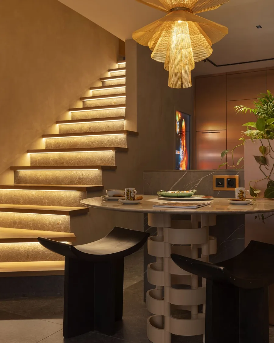 Mesa con pie artesanal, taburetes de madera y escalera iluminada en el showroom de Ritual