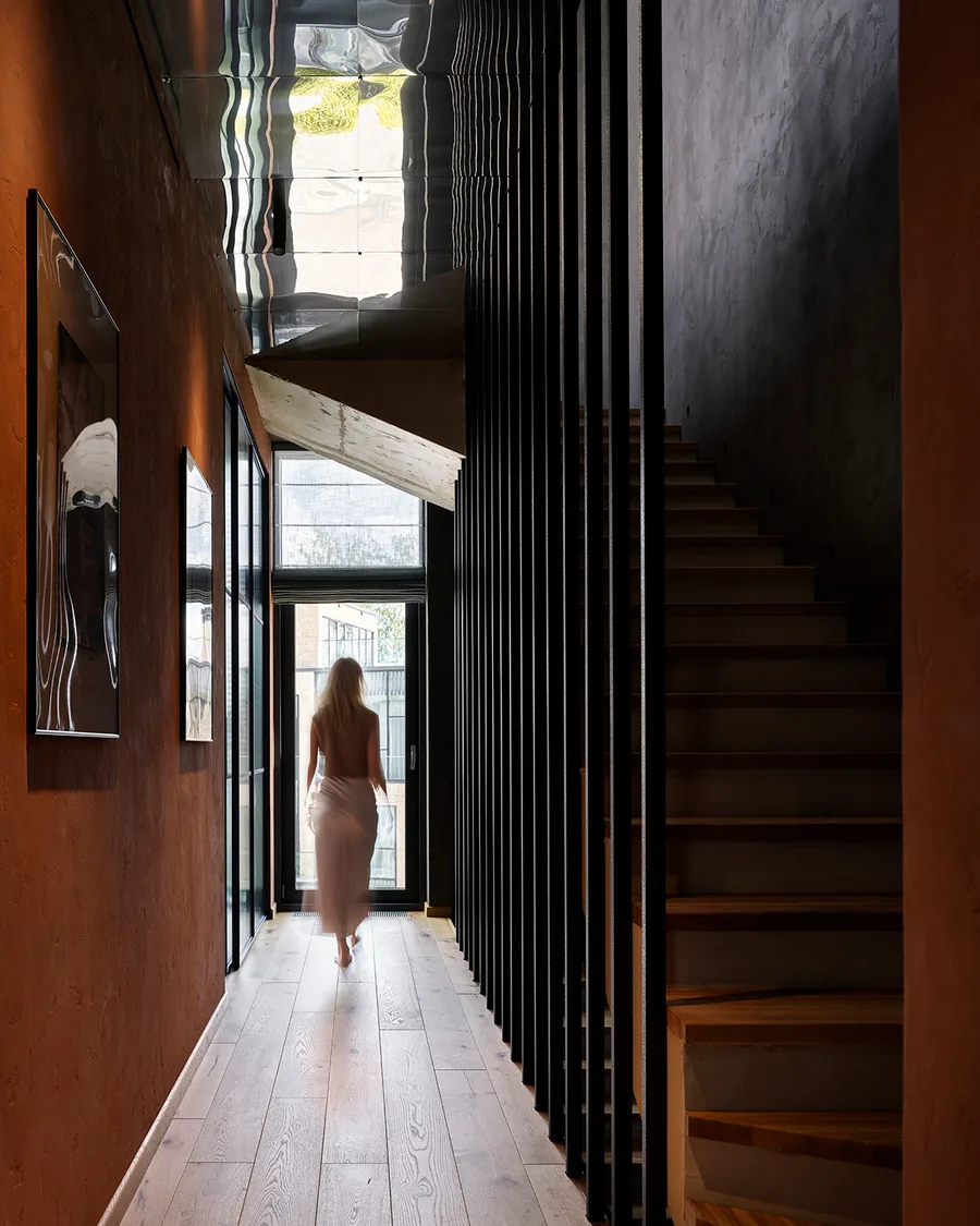 Pasillo con escalera de madera y lamas oscuras que dejan pasar la luz