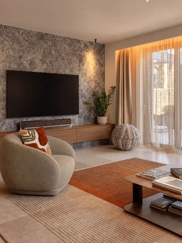 Salón con butaca curva y pared de piedra junto al televisor en Sarrià