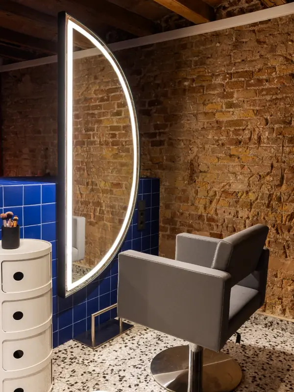 Puesto de peluquería con espejo iluminado y ladrillo visto en Hair Cut Day Letamendi, Barcelona